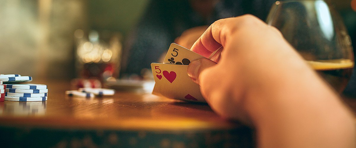 Texas Hold'em Poker, Spieler an einem Tisch mit Karten in der Hand und Pokerchip auf dem Tisch.